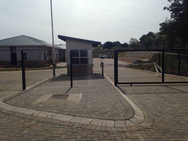 Guardhouse with a black mesh sliding gate across a paved entrance
