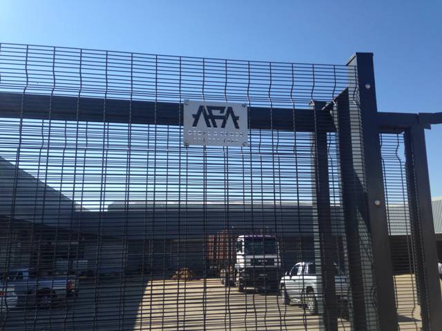 Tall black high-security mesh fence and gate with an AFA sign, trucks parked behind