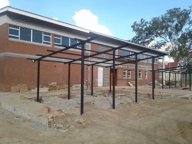 Steel frame of a covered walkway going up along a brick building