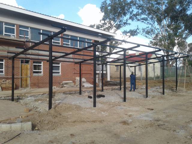 Dark steel canopy columns and beams in front of a brick building